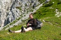 Young woman summerÃÂ hiker with backpack looking at smart watch after hike. Female trekker relaxing on grass in Karavanke mountains